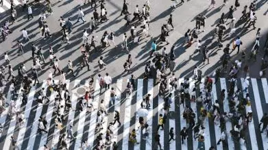 A birds-eye view of lots of people walking across a busy road junction