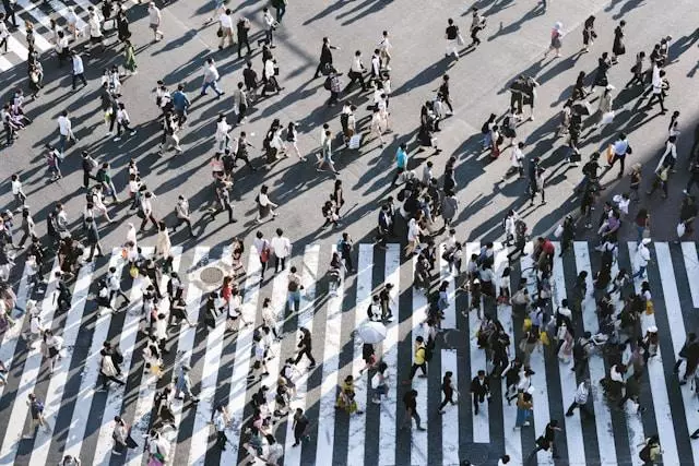 A birds-eye view of lots of people walking across a busy road junction